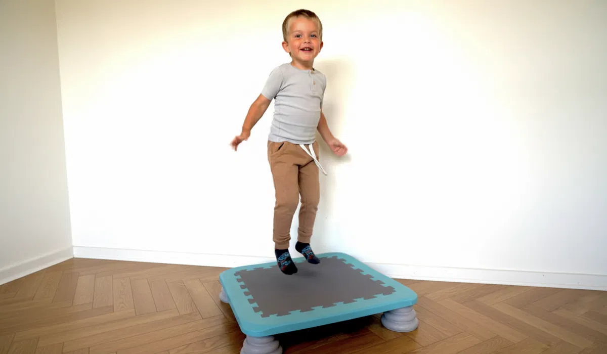 Glad lille dreng der hopper på en blå sansetrampolin for at styrke motorik og balance.